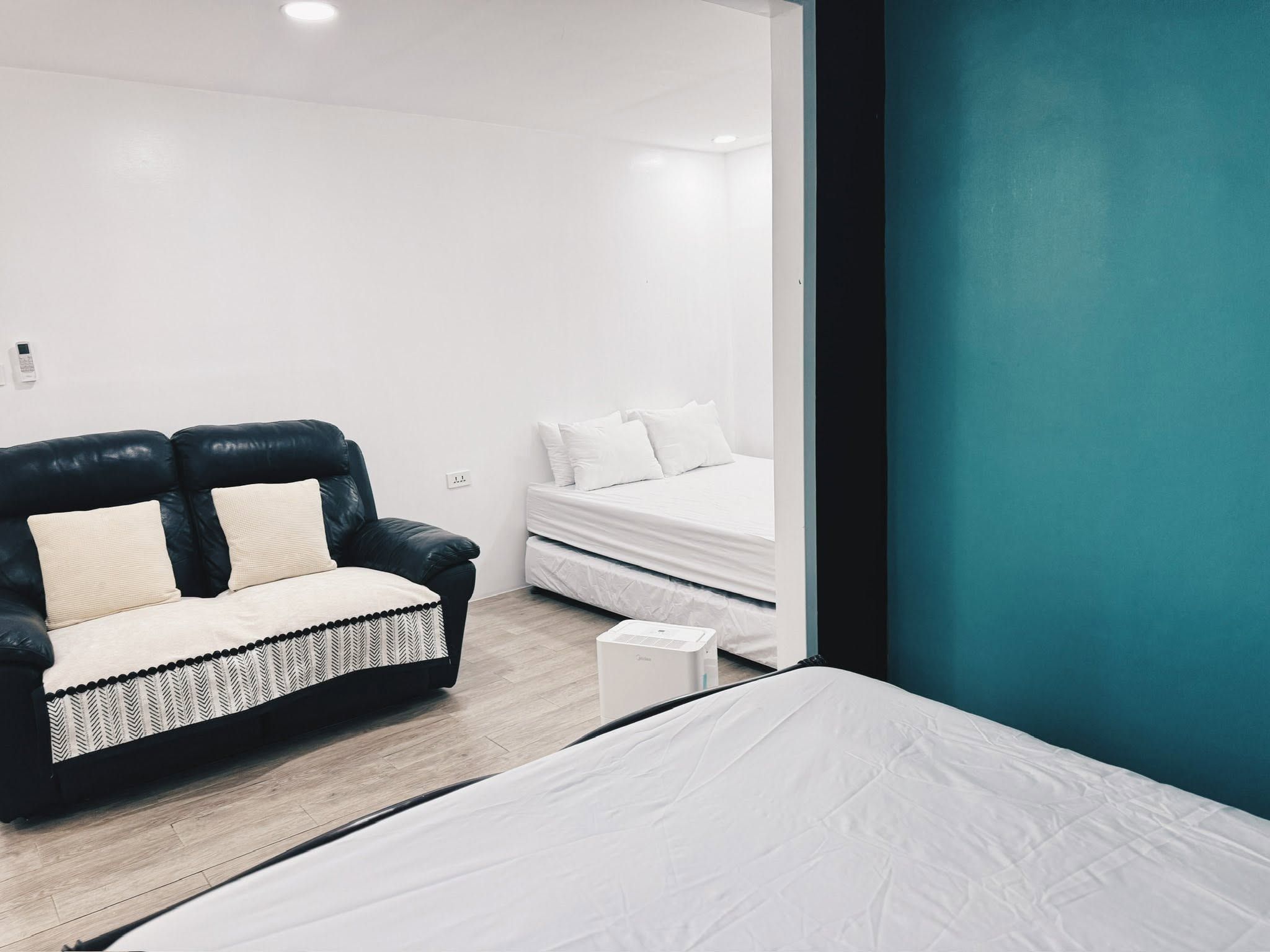 Bedroom with white-dressed beds, a leather loveseat and a teal wall
