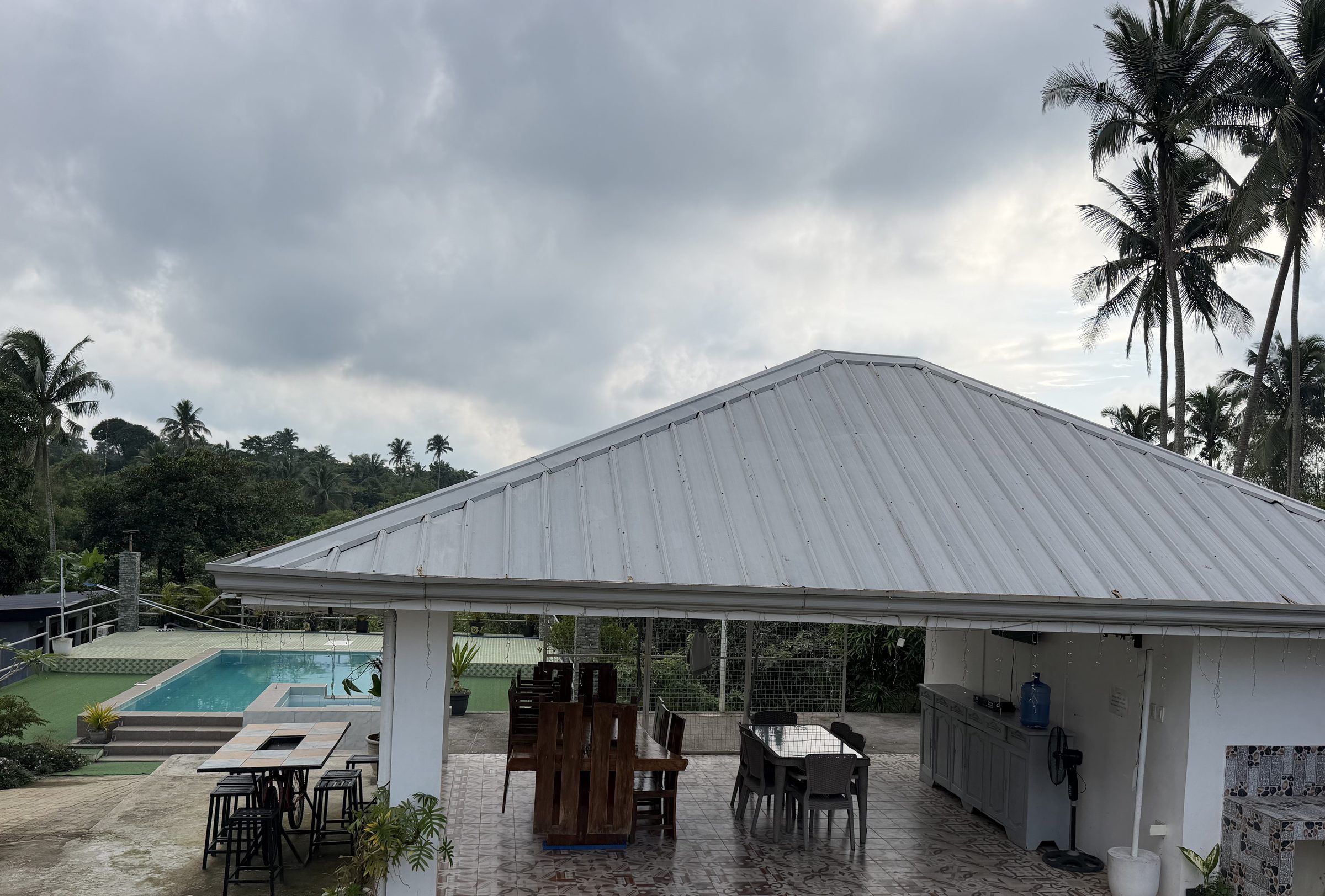 The open-sided dining pavilion with its wooden tables and a kitchen counter, looking across to the pool and the trees beyond