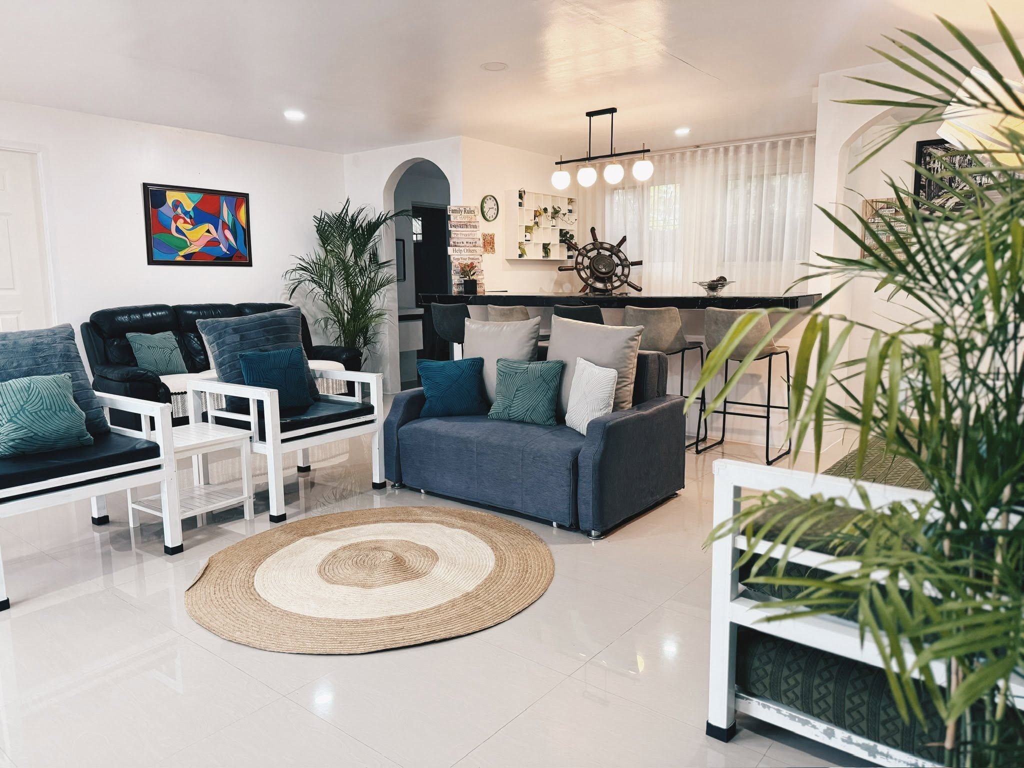 Open living room with white-framed chairs, a navy sofa, a round jute rug and the bar counter behind