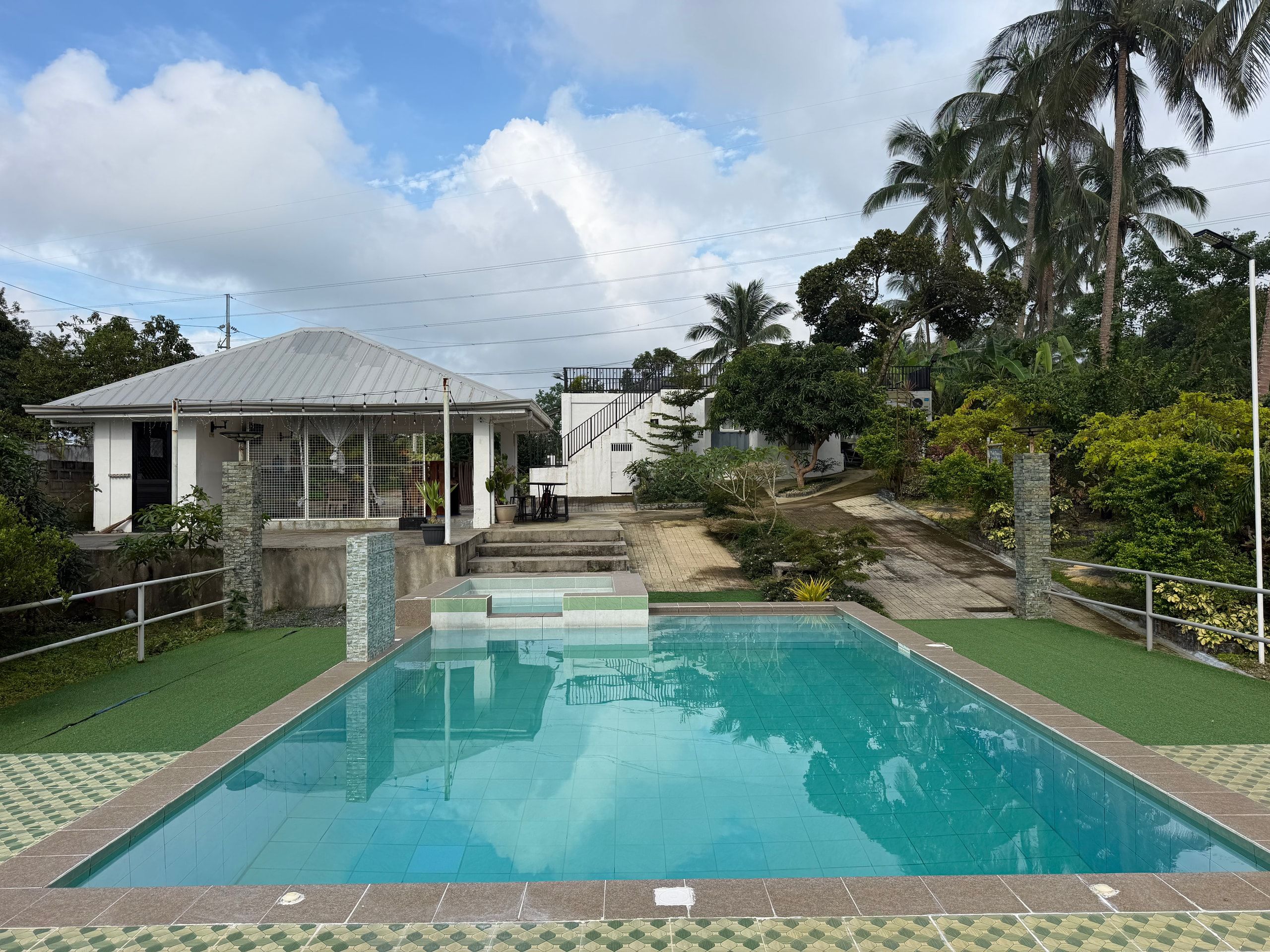 The pool and raised kiddie pool, with the dining pavilion and the main house behind under a blue sky